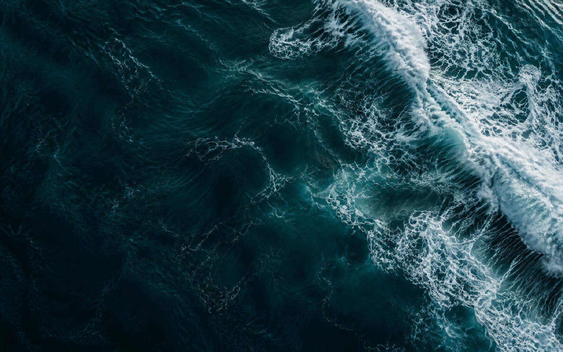 Aerial view of deep teal ocean currents and white surf